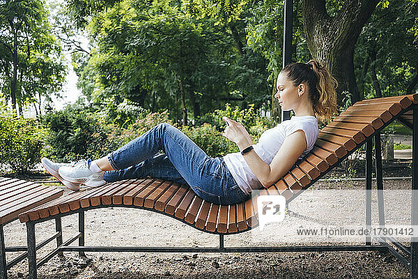 Woman using mobile phone relaxing on deck chair in park