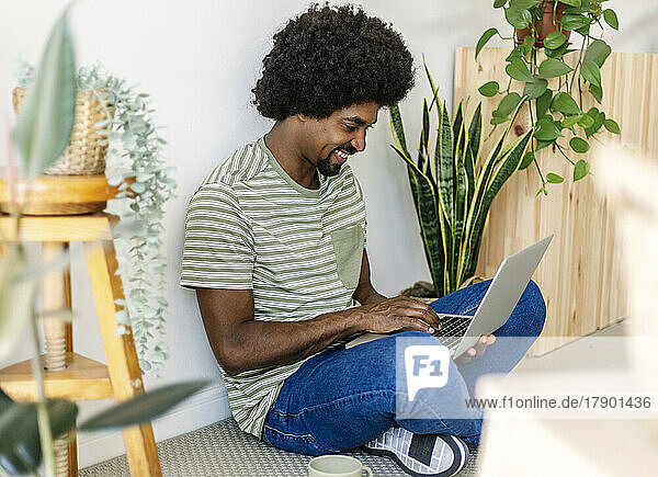 Glücklicher afrikanischer Mann  der zu Hause einen Laptop benutzt
