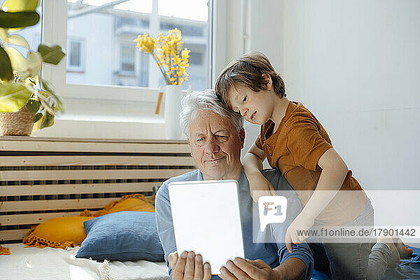 Älterer Mann macht Selfie mit Enkel über Tablet-PC im Wohnzimmer