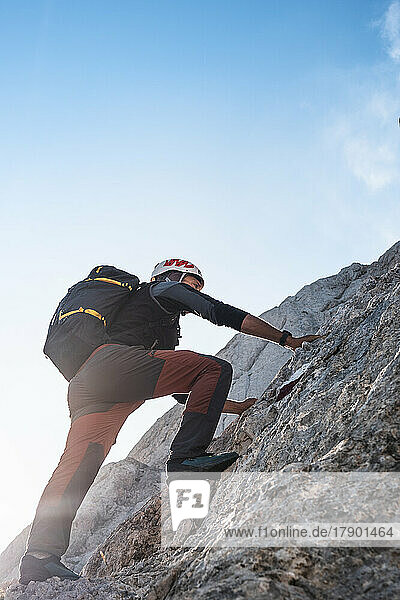 Mountaineer climbing on rocky wall under blue sky