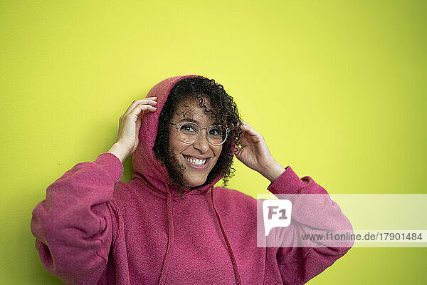 Happy woman wearing hooded shirt in front of green wall