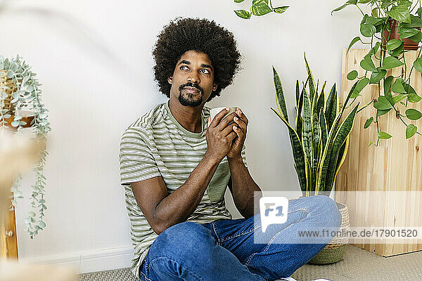 African man with coffee cup sitting in front of wall at home
