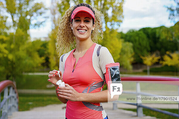 Happy sportswoman holding wireless in-ear headphones in park