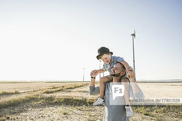 Father carrying son on shoulders in front of wind turbines