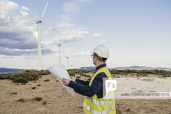 Engineer holding blueprint looking at wind turbines at wind farm