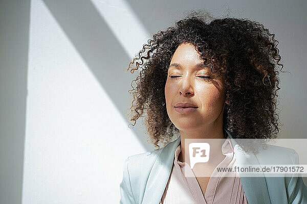 Businesswoman with sunlight on face in front of wall