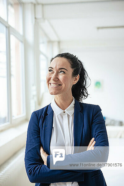 Happy businesswoman standing with arms crossed by window