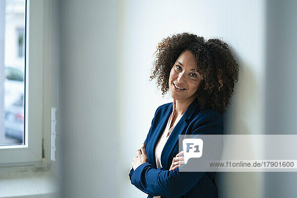 Smiling businesswoman with curly hair leaning on wall