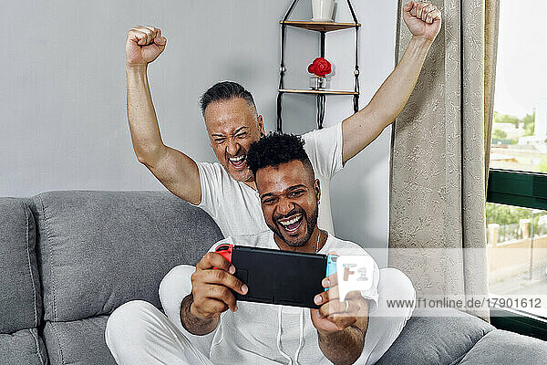 Reifer Mann jubelt seinem Freund zu  der zu Hause ein Videospiel spielt