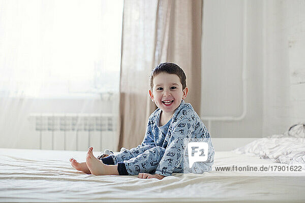 Happy cute boy wearing pajamas sitting on bed