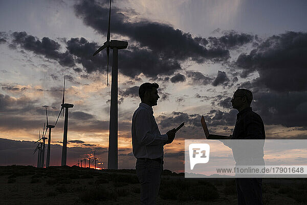 Ingenieure diskutieren bei Sonnenuntergang mit Laptop im Windpark