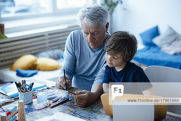 Älterer Mann zeichnet zu Hause auf Tablet-PC von Enkel