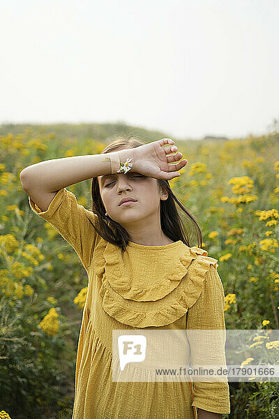 Girl with flowers taped on hand by bandage standing in field