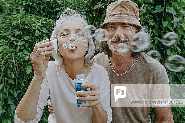 Mature woman making bubbles by senior man in park