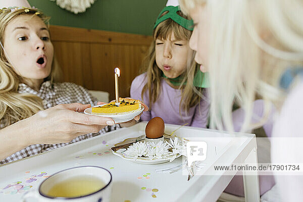 Mutter und Töchter blasen gemeinsam Kerze auf Kuchen