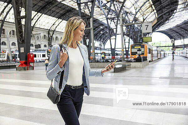 Businesswoman walking with smart phone at railroad station