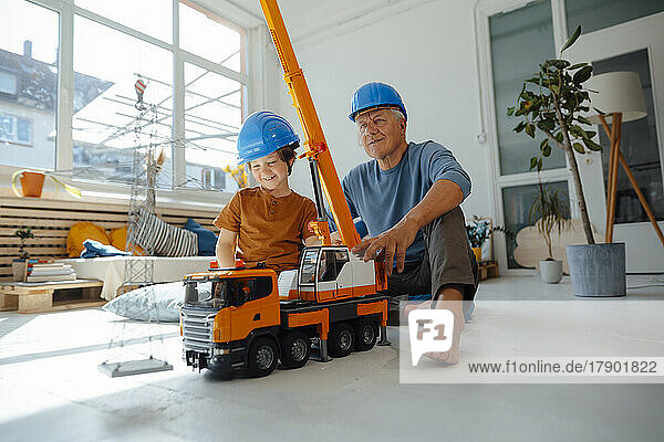 Lächelnder Enkel und Großvater in Schutzhelmen mit Spielzeugkran und Strommastmodell zu Hause