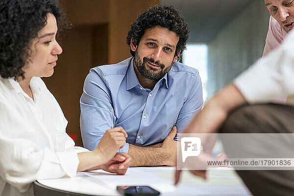 Smiling businessman sitting by colleagues in meeting at office