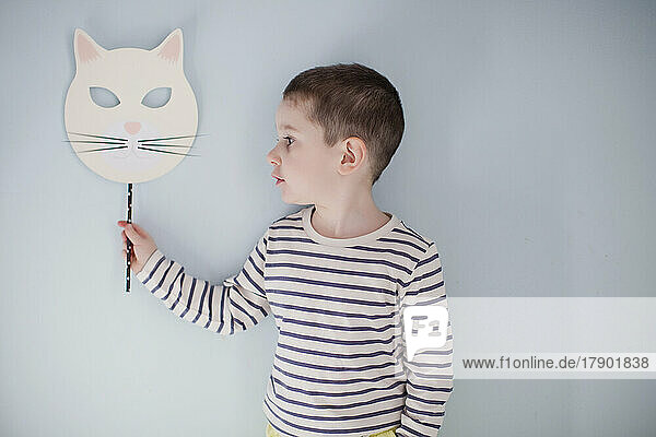Boy standing with Halloween mask in front of gray wall