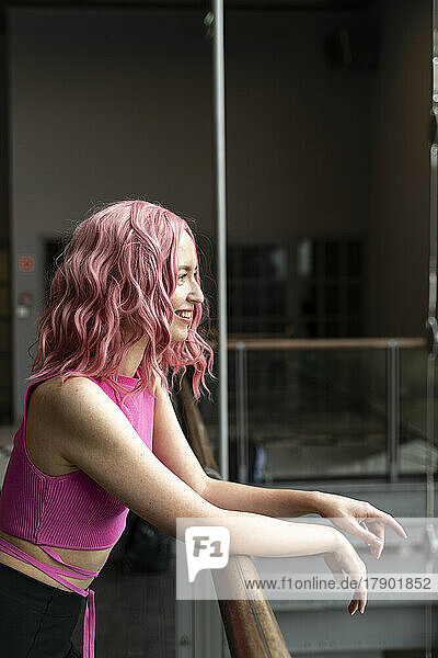 Lächelnde Frau mit rosa Haaren steht am Geländer