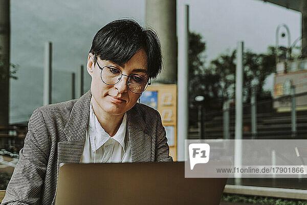 Businesswoman wearing eyeglasses using laptop sitting at sidewalk cafe