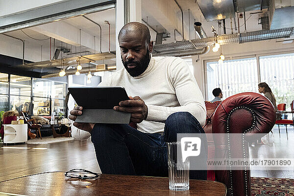 Confident businessman sitting in armchair using digital tablet