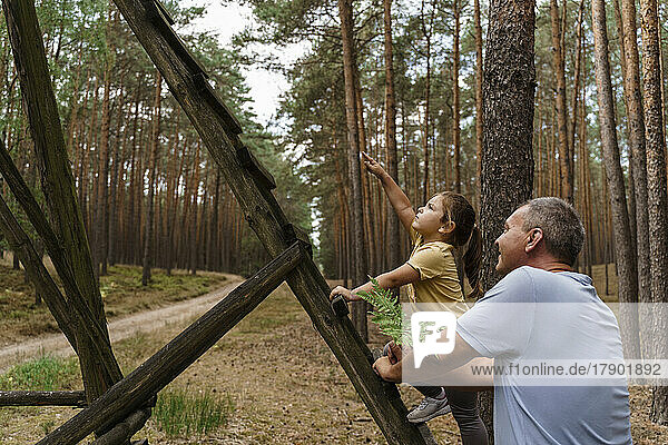 Girl climbing ladder and gesturing to man in forest