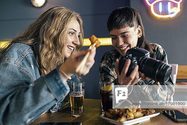 Smiling young lesbian couple with camera sitting at table in restaurant