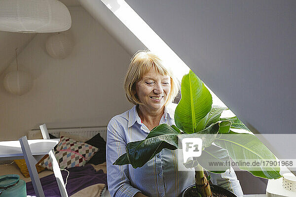 Happy senior woman with banana plant sitting in bedroom