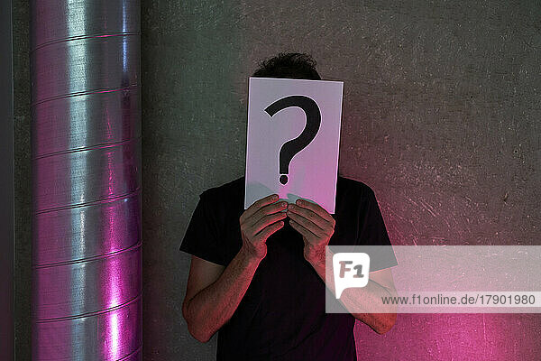 Man holding question mark sign on paper in front of wall