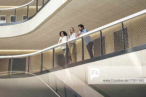 Multiracial business colleague leaning on railing in corridor