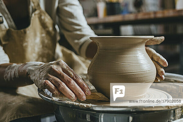 Hands of young potter molding pot shape on pottery wheel
