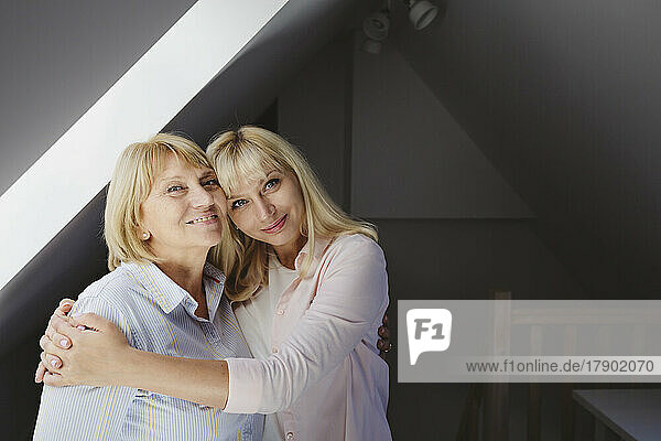 Smiling woman hugging mother standing at home