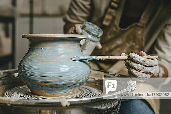 Hand's of potter painting pot on pottery wheel at workshop