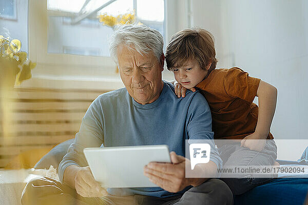 Senior man sharing tablet PC with grandson in living room at home