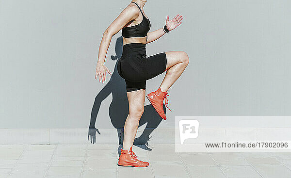 Woman exercising by gray wall on sunny day