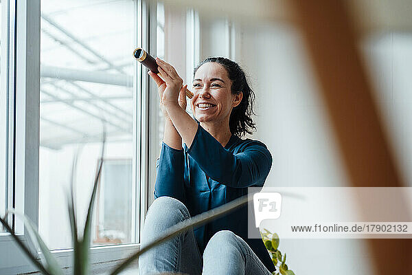 Happy woman holding antique monocular sitting by window