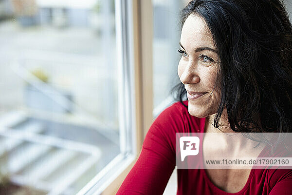 Smiling thoughtful woman looking through window