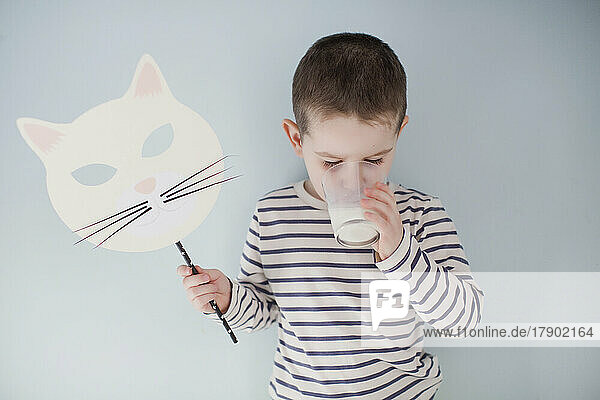 Boy with Halloween mask drinking milk in front of gray wall
