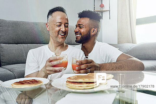 Happy gay couple having breakfast in living room at home