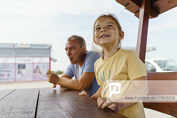 Happy girl sitting with mature man at picnic table