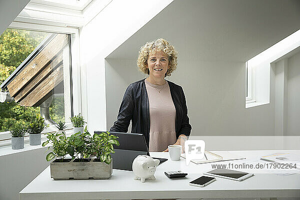 Smiling blond businesswoman standing by desk at home office