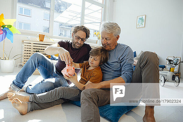 Senior man with son and grandson putting money in piggy bank at home