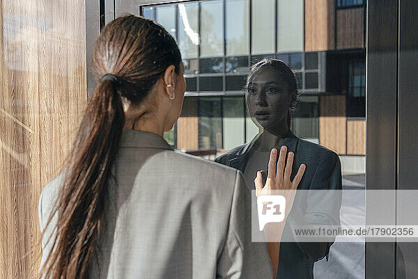 Businesswoman looking at reflection on glass door
