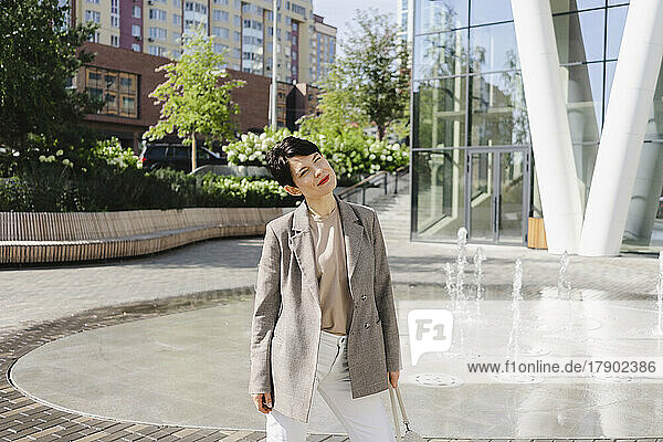 Smiling businesswoman standing in front of fountain at office park