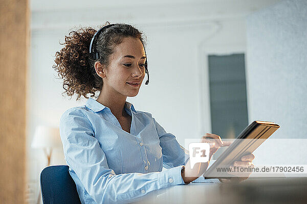 Smiling customer service representative using tablet PC sitting at desk in office