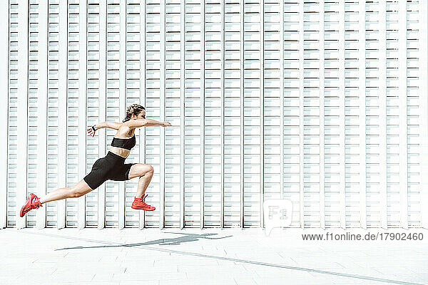 Young athlete jumping by white wall on sunny day