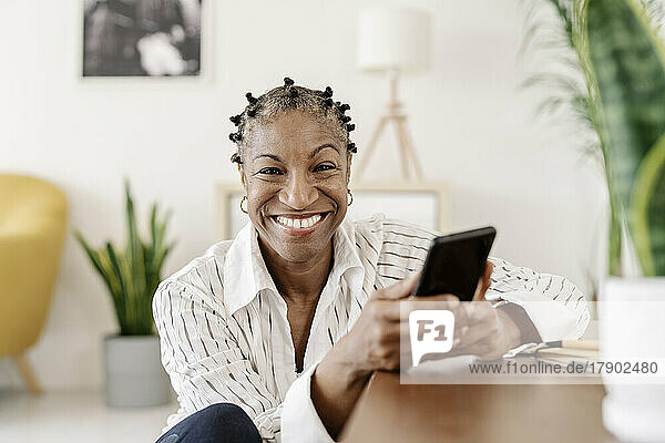 Happy mature woman with smart phone sitting in living room at home