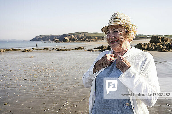 Glückliche ältere Frau mit Hut im Urlaub am Strand