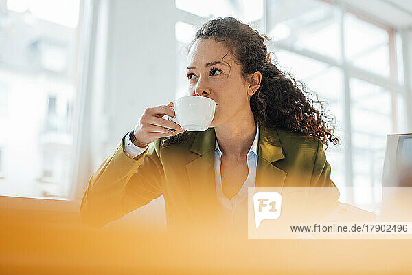 Young businesswoman with curly hair drinking coffee